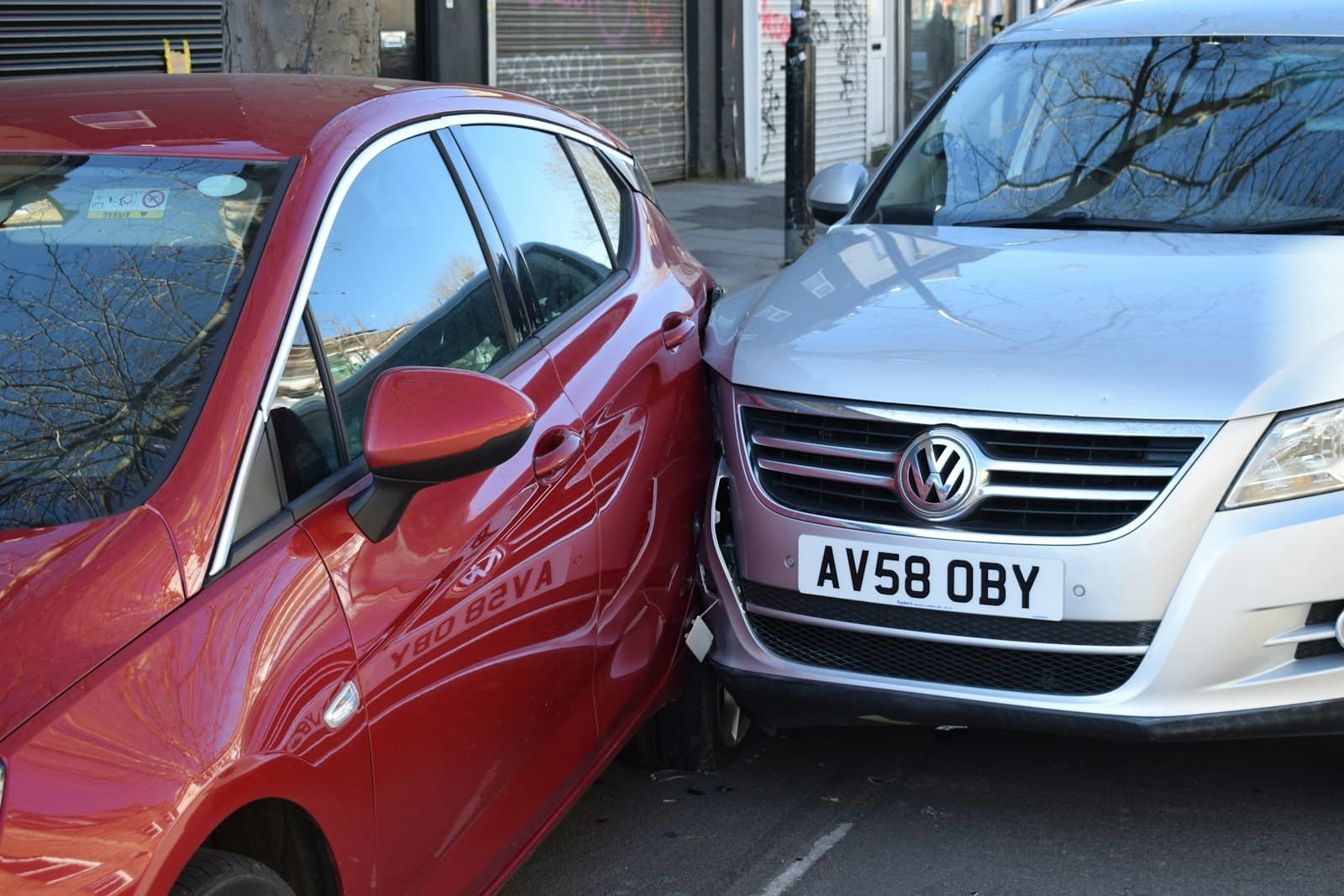 Two-car collision on a city street, a red car's front end crumpled against a white Volkswagen