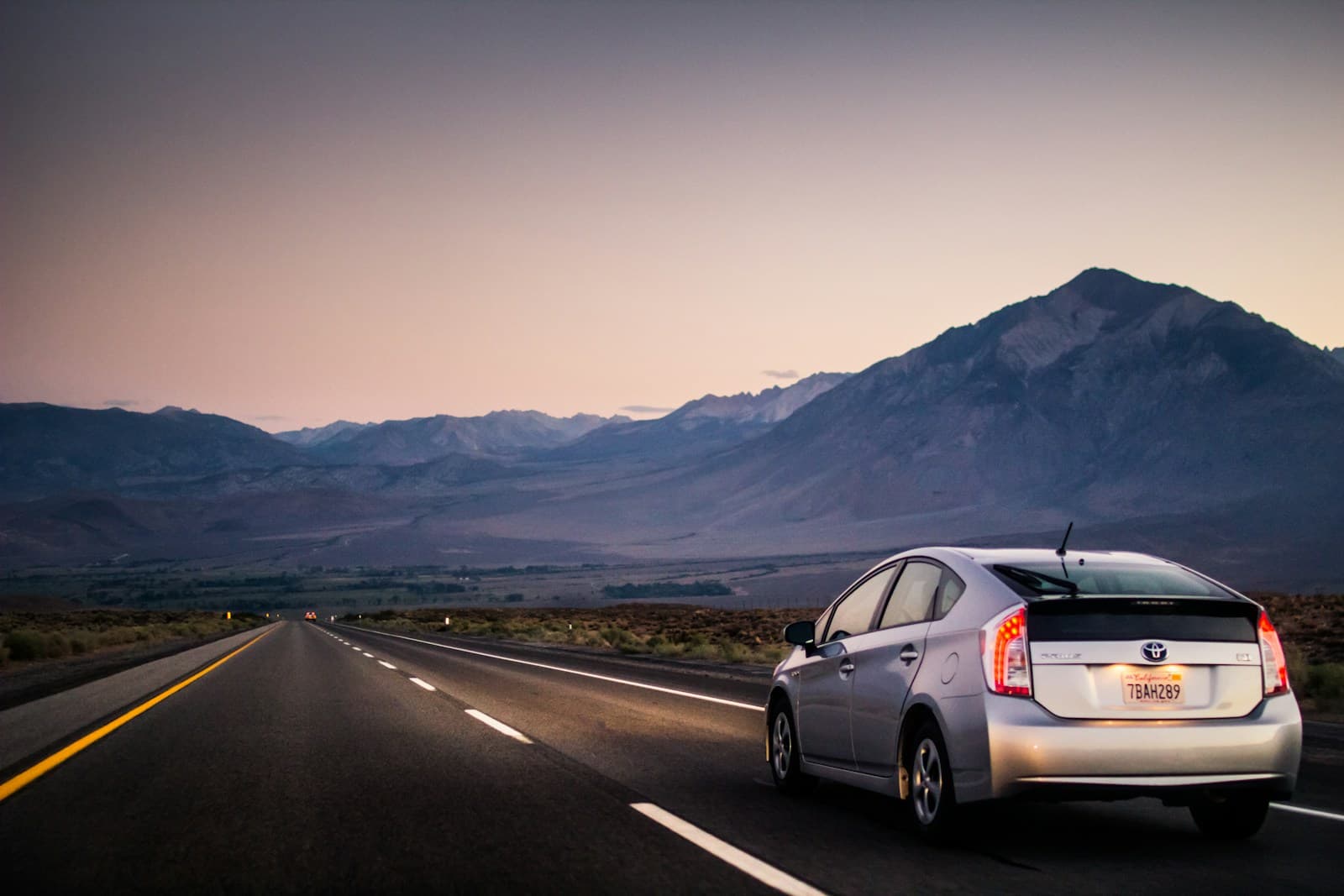 Silver Toyota Prius on a straight desert highway toward mountains at sunset